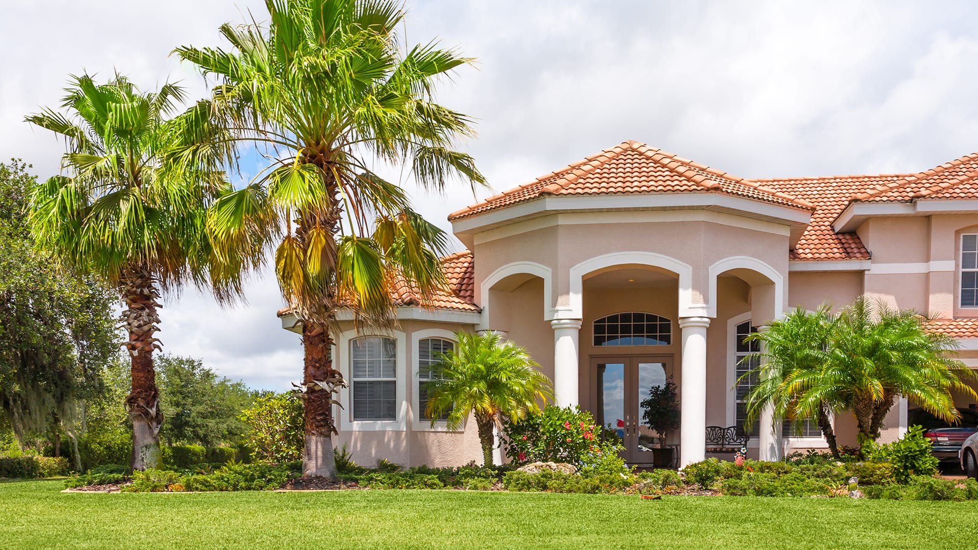 Front of a Florida mansion with palm trees and green grass