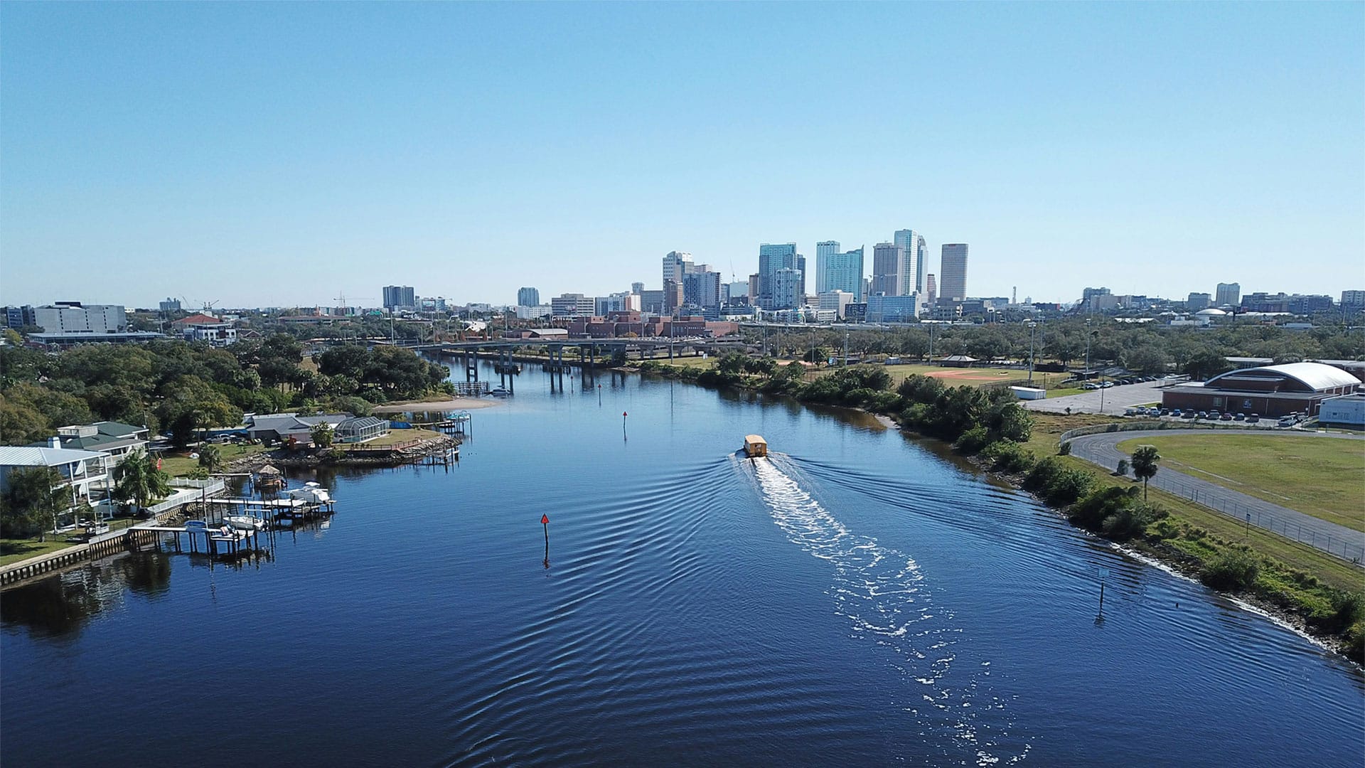 Boat heading down a river with tall office buildings in the distance