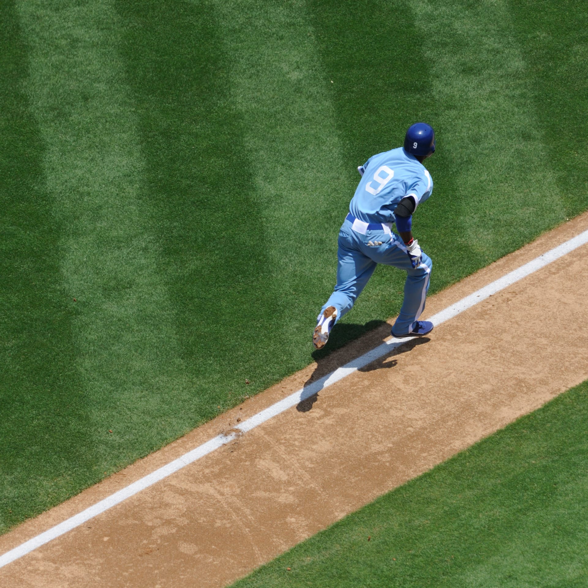 Baseball player running to the next base on a green stripey pitch