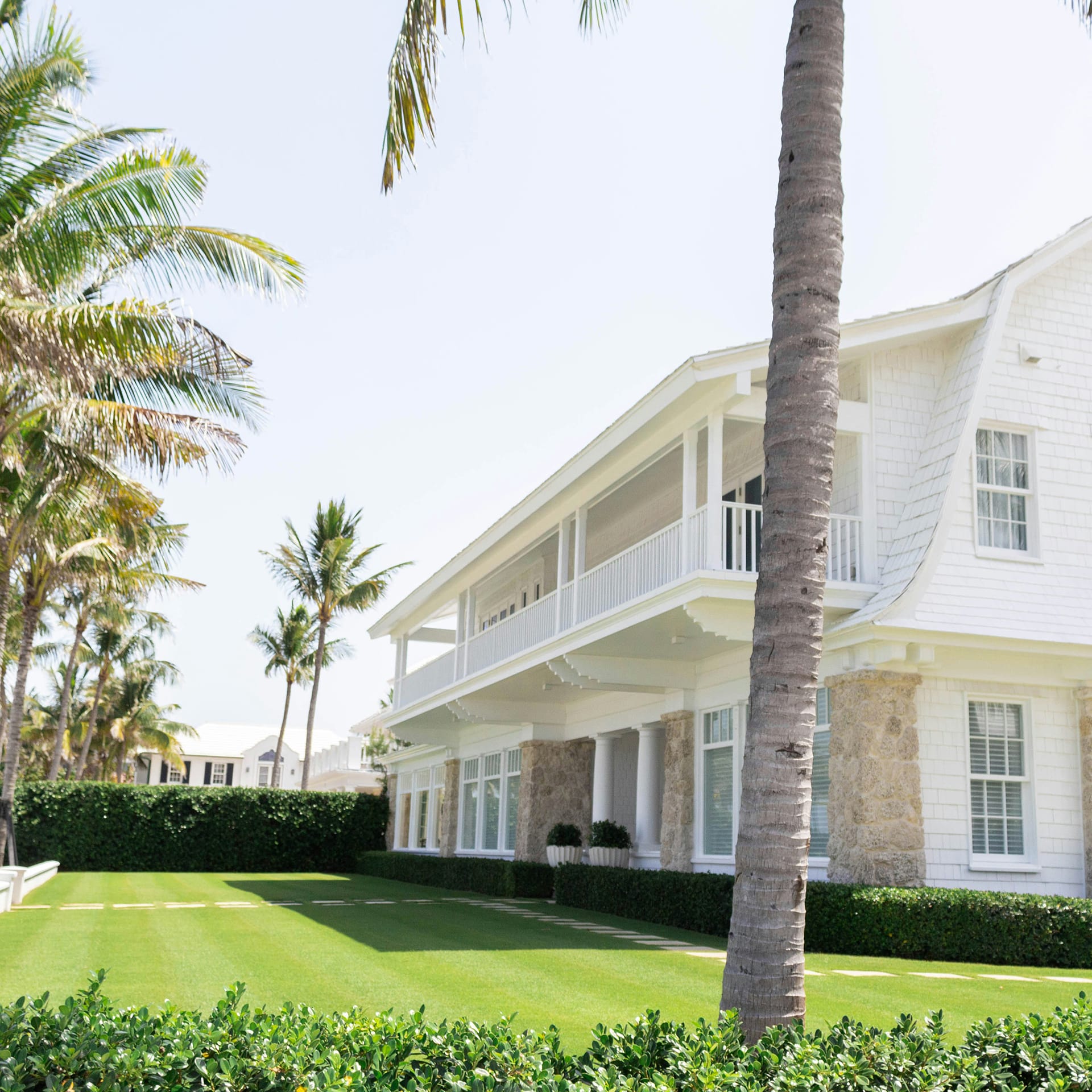 A white house with balcony looking out onto a green garden with palm trees
